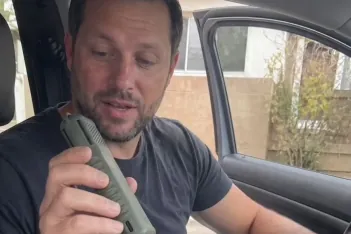 A man in the driver's seat of a vehicle holding up a MoskiCell unit